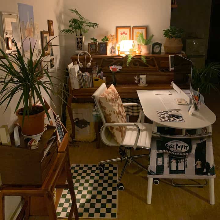 Warm wood tone natural study with white desk and chair, assorted plants and picture frames creating a cozy home office