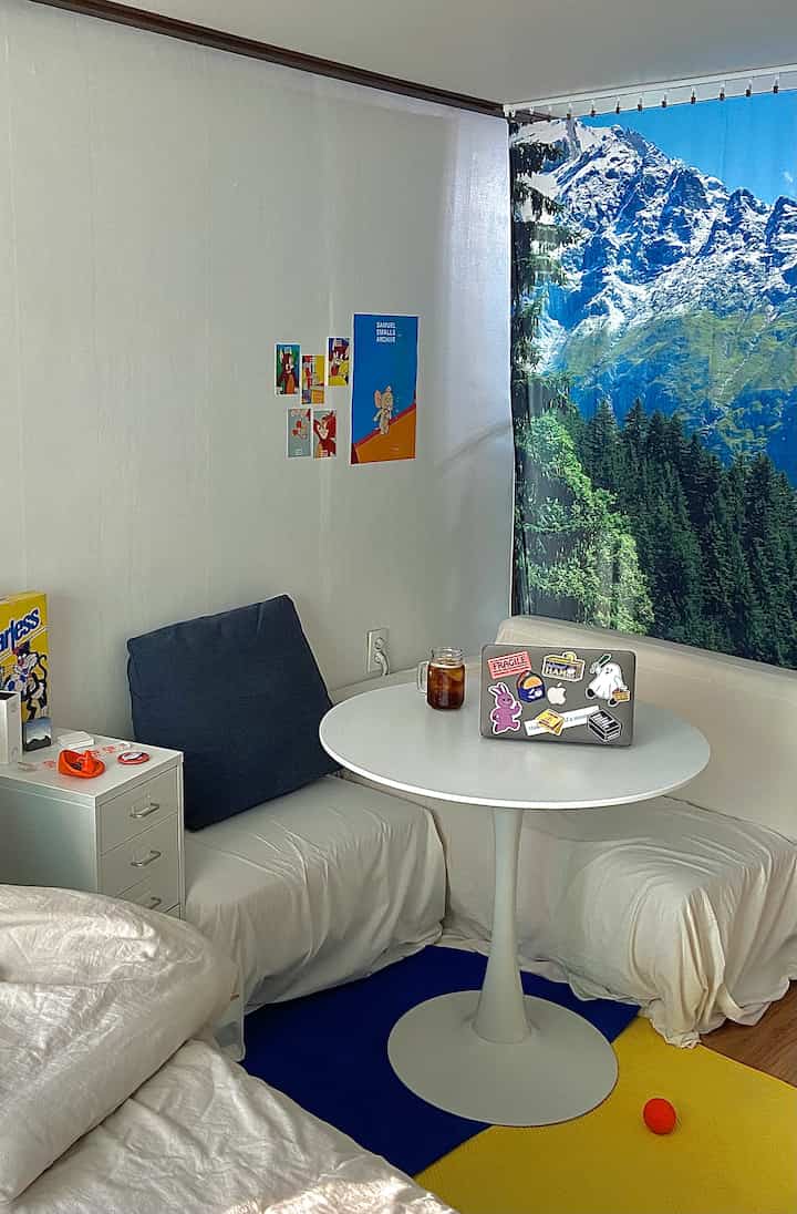A small studio bedroom with white and blue tones featuring a round dining table and fabric-covered sofas in a tidy setting
