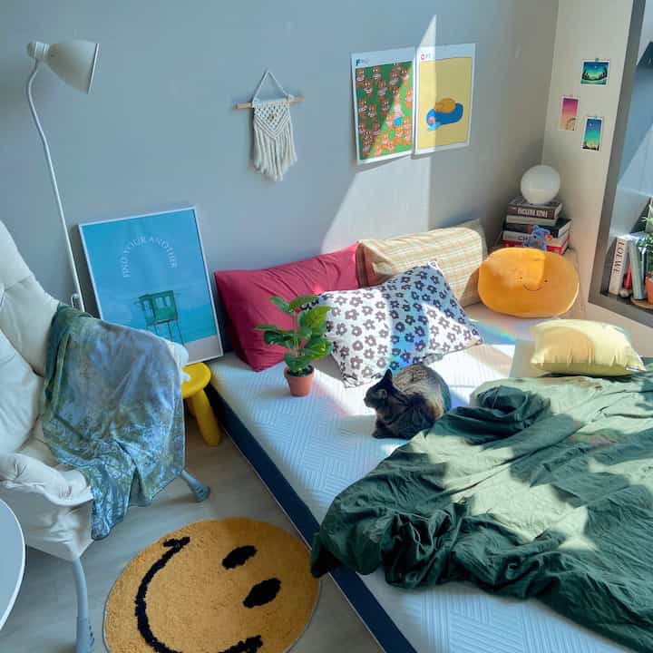 ナチュラルな色調の寝室、白いマットレスベッドにダークグリーンの掛け布団、そしてタビー猫が座る居心地の良いインテリア