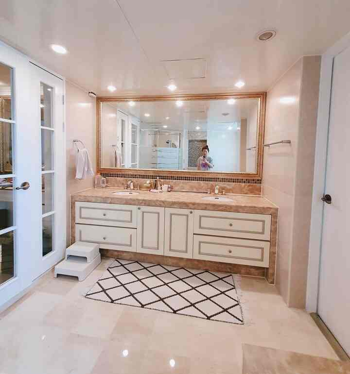 Spacious bathroom in beige and white tones, featuring large double vanity and patterned rug creating tidy atmosphere
