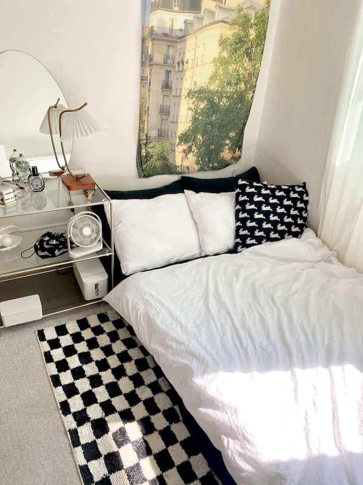 A modern bedroom in white and black tones featuring an arch mirror and checkered rug, bathed in soft natural light