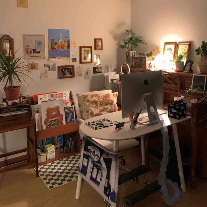 Warmly lit natural-style study featuring a white desk with iMac, framed pictures, and plants creating a cozy home office atmosphere