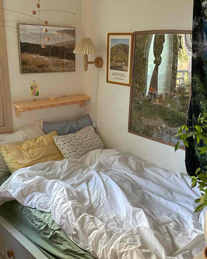 White and green toned bedroom featuring neat duvet cover and cushions, natural wood picture frames and lamp creating a cozy atmosphere