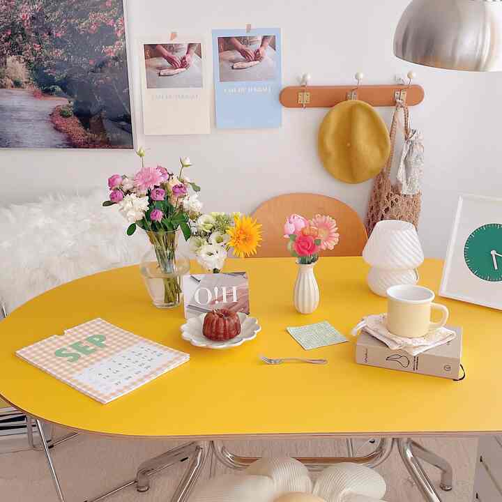 Bright yellow-toned dining room featuring a table with flower vases and mini dessert, complemented by a wall-mounted coat rack for a cozy vibe