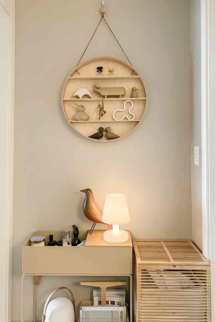 Beige and wood tone restroom entryway featuring a round shelf with wooden figurines and a table lamp, creating a natural and cozy atmosphere