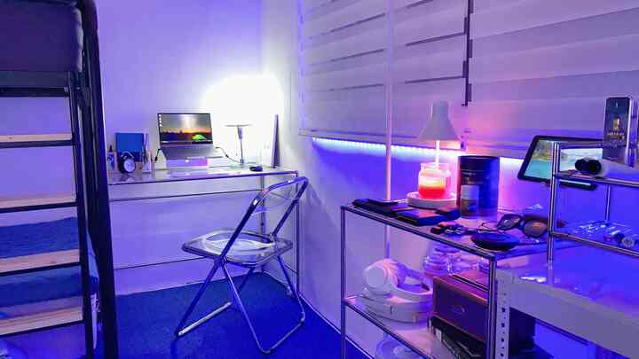 Blue and white toned studio apartment home office featuring a transparent chair and metal shelving, compact modern atmosphere