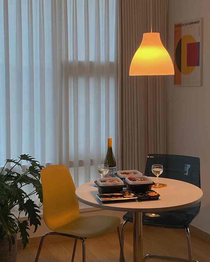 Mid-Century Modern dining room featuring white round table and colorful dining chairs with warm wood tone flooring under soft pendant lighting