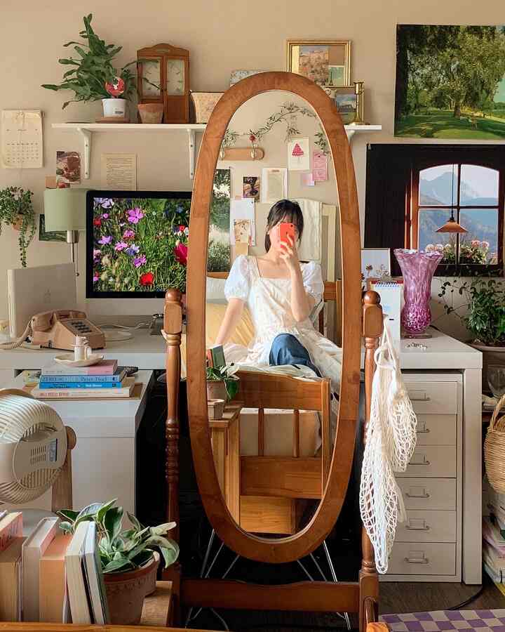 Small bedroom with dominant wood tones and natural colors, featuring a full-length mirror, desk, and plants creating a cozy atmosphere