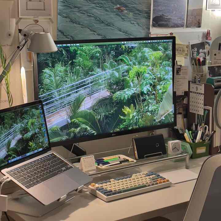 White-toned study space featuring a large monitor, MacBook, and organized desk accessories creating a neat workspace