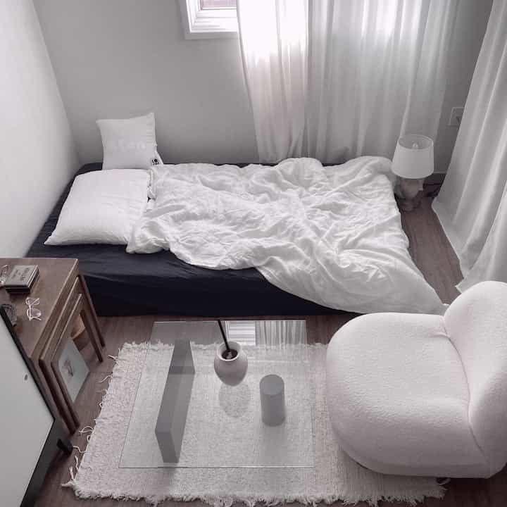Calm navy and white toned studio bedroom featuring a bed, sofa, side table with a clean natural modern atmosphere