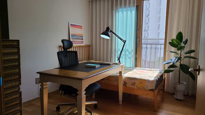Natural wood tone and white-walled single household bedroom featuring a desk and office chair in a neat home office setup