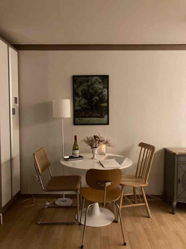 ナチュラルで木目調の小さなダイニングルーム、白い丸テーブルと3つの異なる木製ダイニングチェアが配置された空間