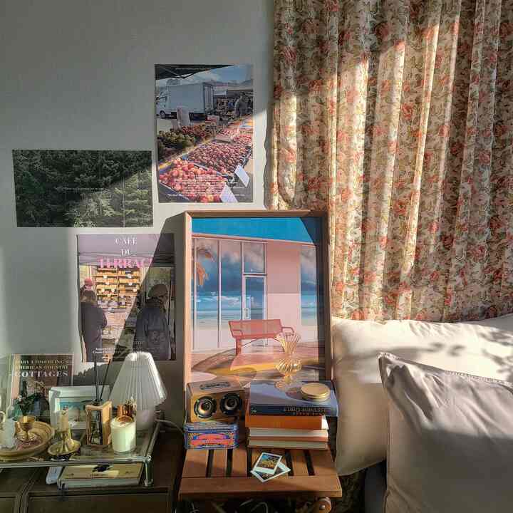Sunlit bedroom featuring floral curtains, wood tone nightstand, picture frames, and posters
