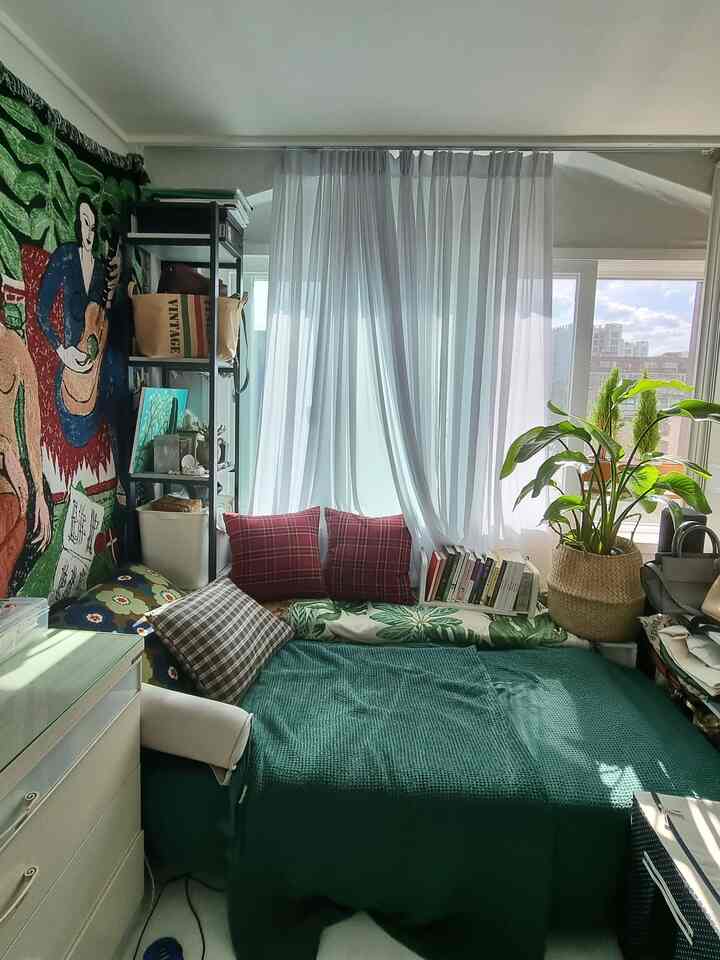 緑色のトーンとヴィンテージ壁画を背景にした日差しの明るいリビング、ソファベッドと大きな観葉植物が配置された印象的な空間