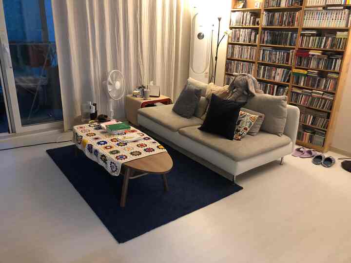 白い床とネイビーブルーのラグのあるリビング、ソファとコーヒーテーブルが配置されたシンプルな空間