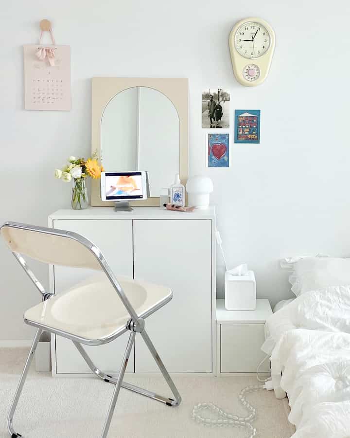White and beige toned bedroom featuring a vanity with a folding chair, creating a neat and minimalistic atmosphere