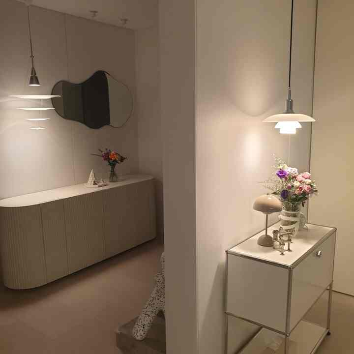 落ち着いた白のトーンの玄関、ルイスポールセンのペンダントライトとミニマルな収納が配置されたギャラリー風の空間