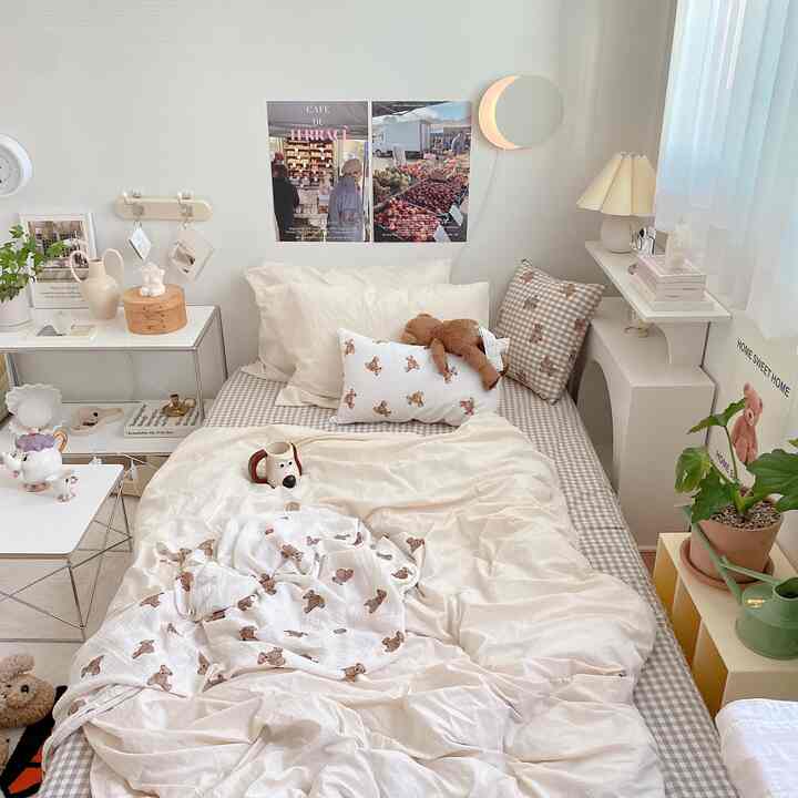 Cozy bedroom in soft beige and white tones featuring a bed with bear plush toys and cushions, complemented by plants in a natural style