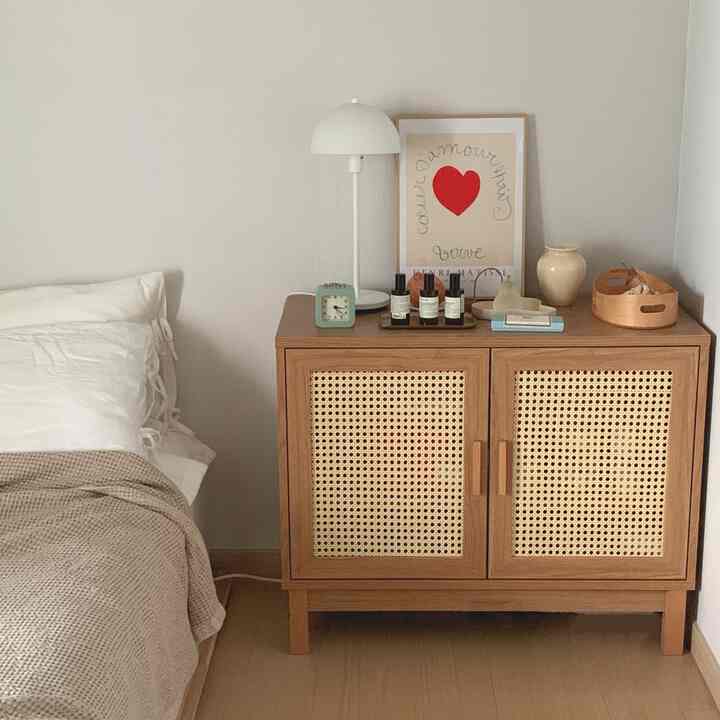 A white and brown toned bedroom featuring a rattan door nightstand and pillows in a cozy setting