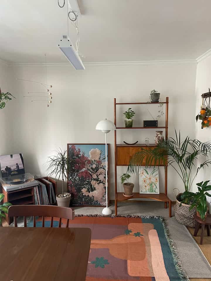 白い壁と木目調家具のダイニングルーム、多様な植物とカラフルなラグが印象的なナチュラルモダンなインテリア