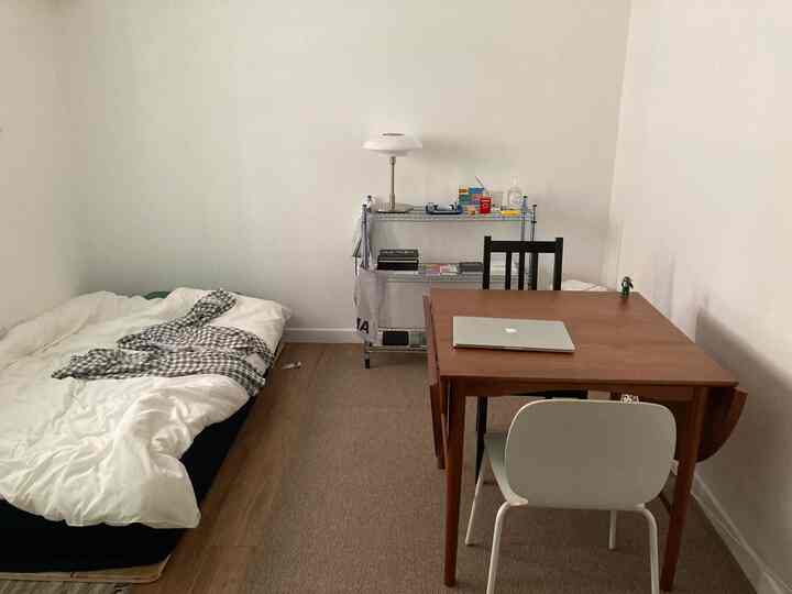 Compact single-bedroom space with white walls and wood-tone table creating a natural vibe in a small apartment
