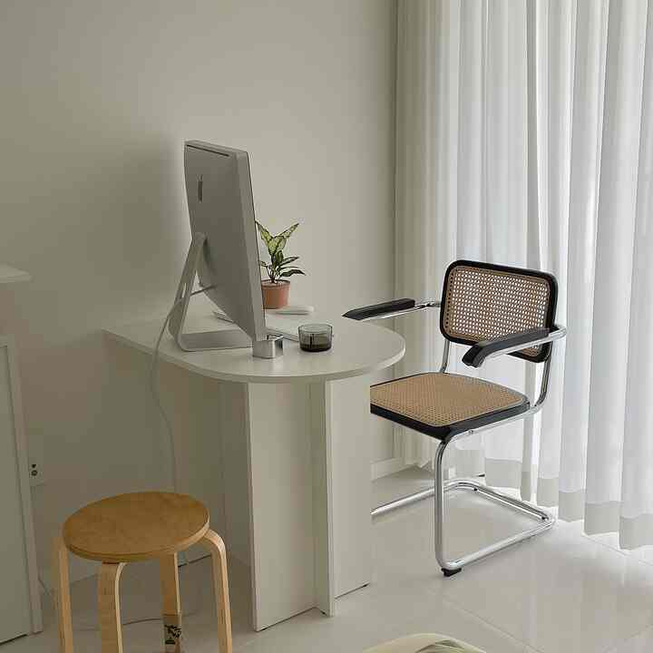 White-toned home office space featuring a rattan armchair and wooden stool with a simple, natural atmosphere
