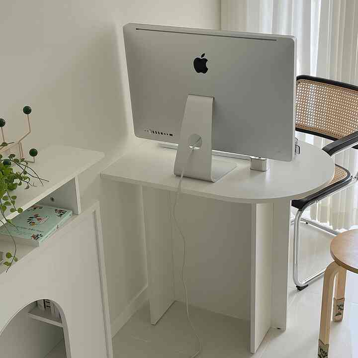 White-toned home office space with natural materials, featuring a half-oval desk with Apple iMac and armchair in a simple interior
