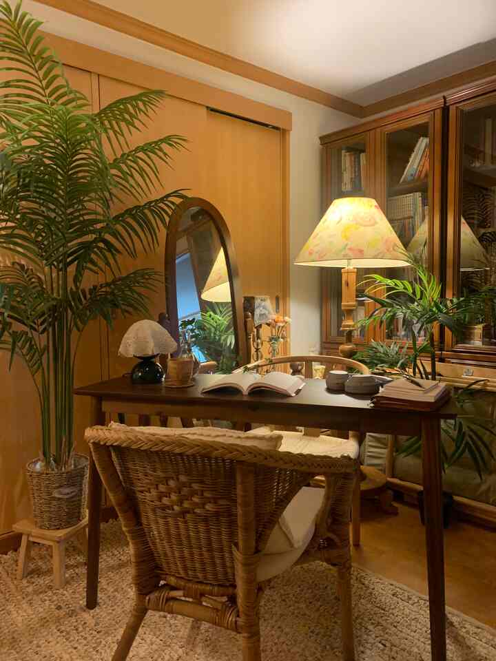 温かみのある木目調とラタンチェアが配された落ち着いた書斎、デスク上の照明と植物が特徴的なインテリア