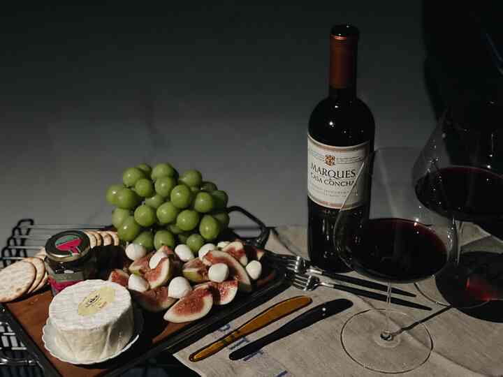 Dark-toned home bar featuring wine glasses, wine bottle, cheese, grapes, and figs on a serving tray with cutlery