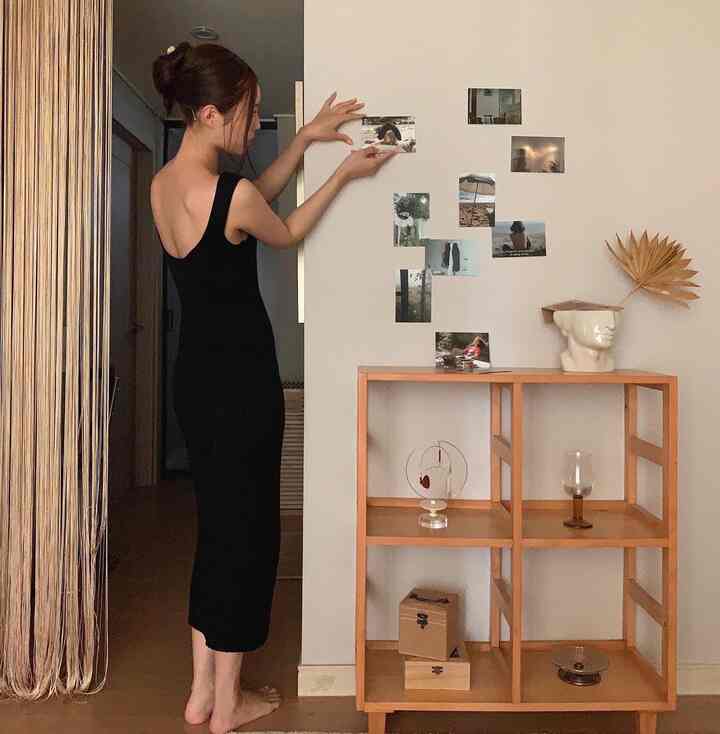 白い壁に写真ポスターが貼られ、木製の棚に陶器の花瓶とドライフラワーが置かれた、自然な雰囲気の寝室空間