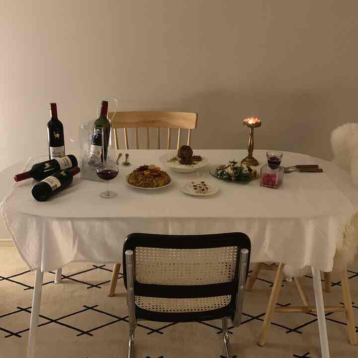 Warm natural-tone living dining room featuring white dining table, wooden chairs, wine bottles, dishes, and cozy ambient lighting