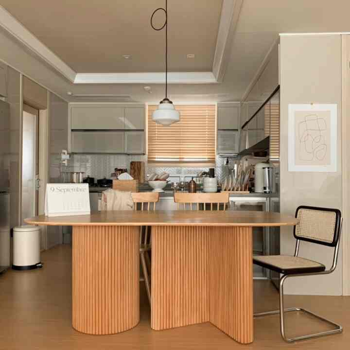 暖かみのある木目調とホワイトが調和したキッチン空間、中央に置かれた木製のダイニングテーブルとチェアが柔らかく居心地の良い雰囲気を演出しています。