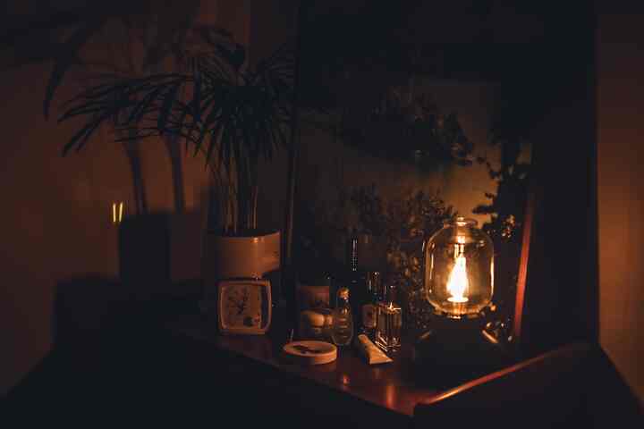 ゴールドの灯りが照らす落ち着いた空間、木目調のナイトスタンドとアレカヤシの植物が配置された雰囲気のあるインテリア