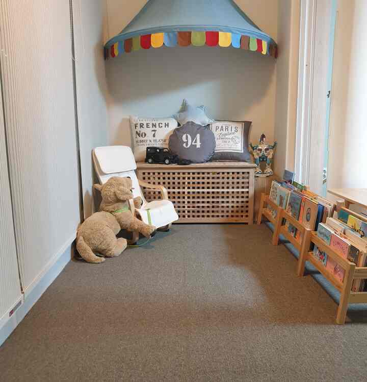 Natural and white toned kids' room featuring a children's armchair, bench, bookshelf, and stuffed dog in a cozy setting