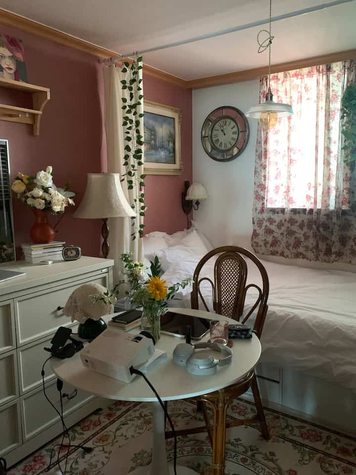 ピンクとアイボリーの色調の寝室、丸テーブルとヴィンテージ風の小物が配置された雰囲気のある空間