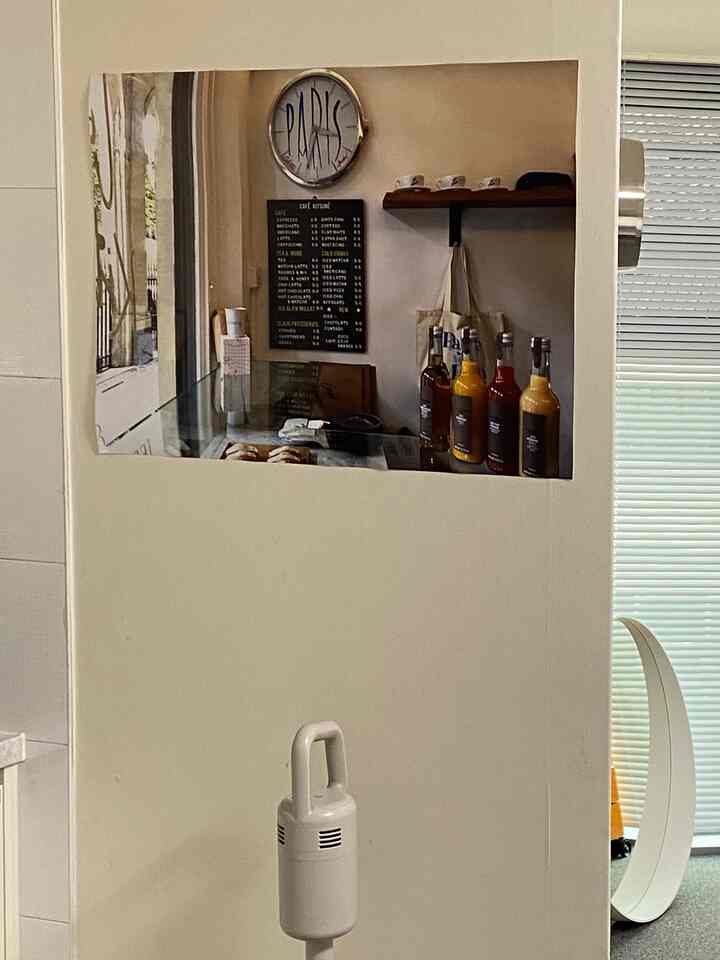 White and beige toned small home cafe kitchen space with menu board, cups and bottles arranged on wall and shelves