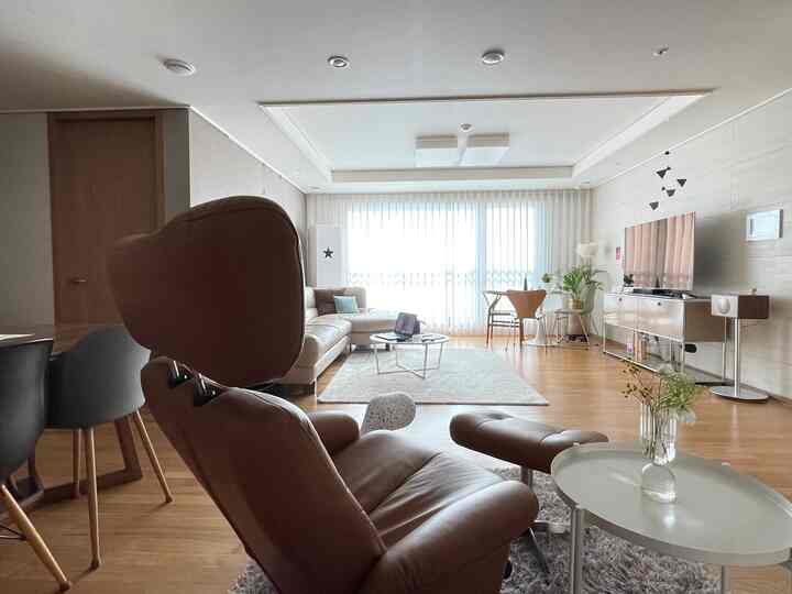 Natural-toned living room featuring a large brown recliner, beige sofa, and white curtains creating a comfortable modern atmosphere
