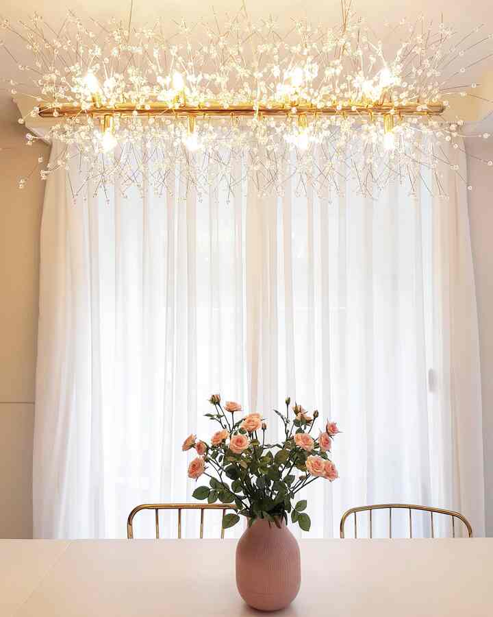 White-toned dining room featuring an extendable white dining table with pink rose bouquet, adorned by sparkling snowflake pendant light overhead in a simple elegant space