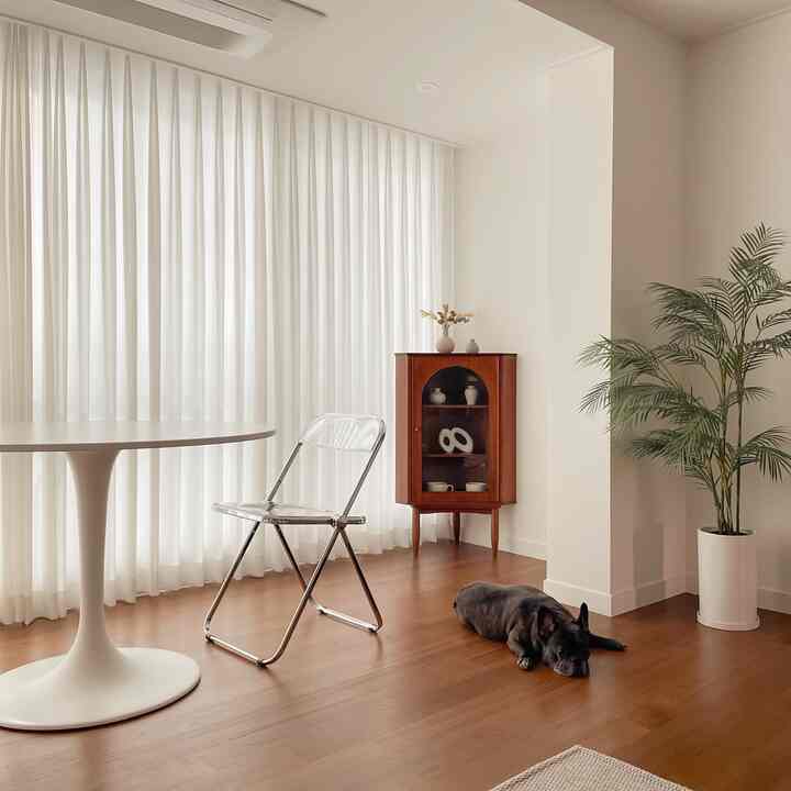 白と木目調が調和するリビング、円形テーブルとコーナーキャビネットが配置されたミニマルで自然な雰囲気のインテリア