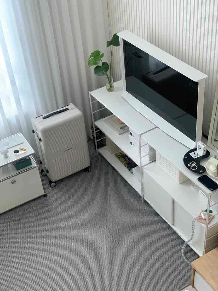 Small single household room in white and gray tones featuring a minimalist white shelving unit and TV stand in a neat interior