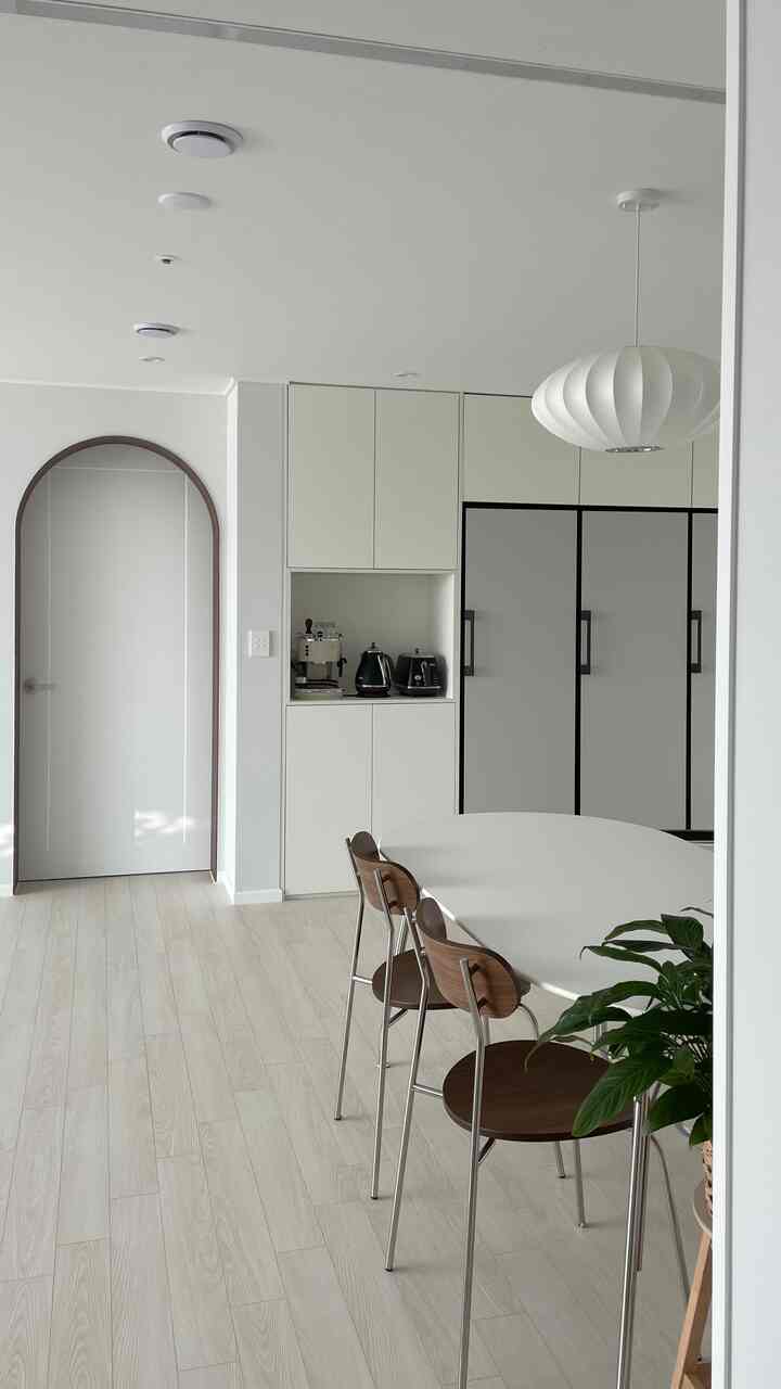 A simple modern entrance space featuring a white kitchen and dining table with wood tones harmoniously combined