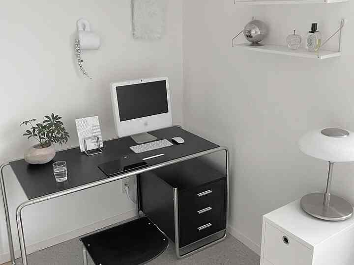 白と黒の配色が特徴的なワンルームのホームオフィス、シンプルでモダンなデスクとスツール、テーブルランプが配置された清潔感のある空間