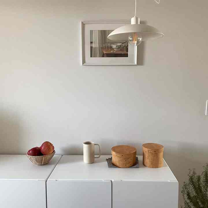 Minimal dining space with white and wood tones, featuring a picture frame and pendant light as focal elements