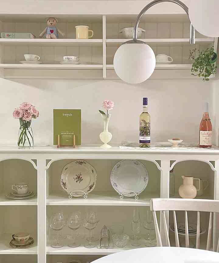 白を基調としたキッチン、ヴィンテージの皿と花瓶、ペンダントライトが配置された雰囲気のあるインテリア