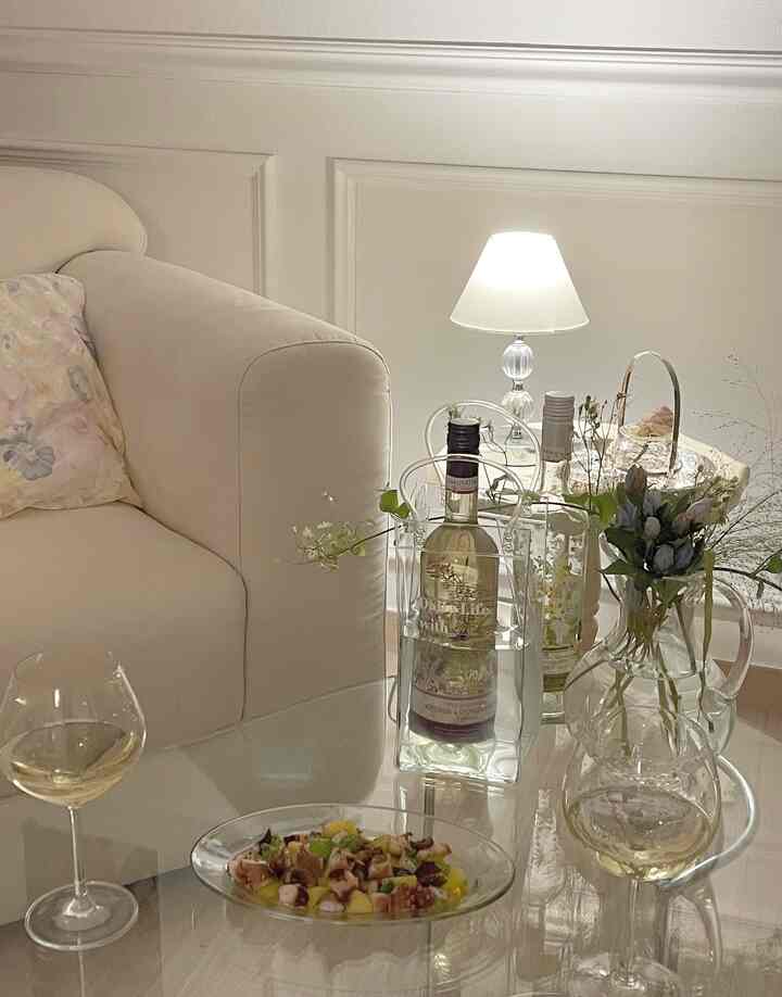 White and natural color living room featuring transparent glass table with wine glasses and bottles creating a cozy atmosphere