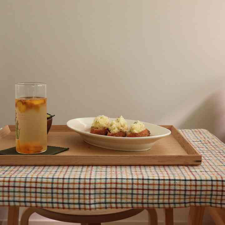 Warm beige-toned table with a checkered tablecloth featuring a wooden tray holding a glass and plate, creating a cozy dining setting