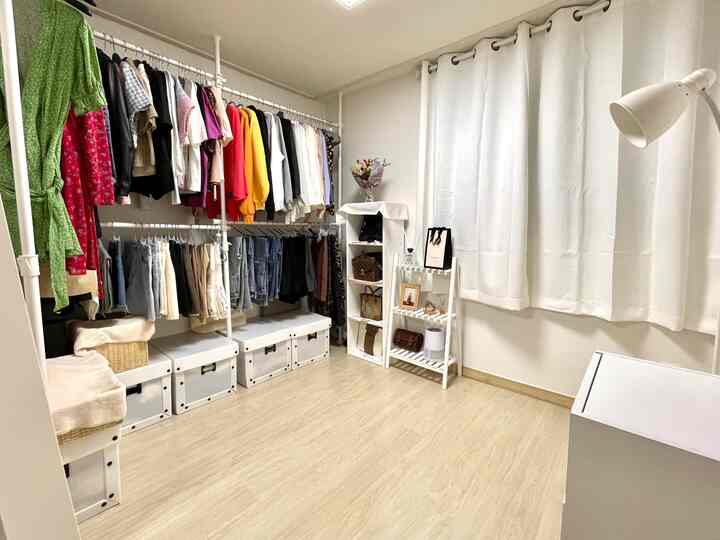 白とナチュラルトーンのウォークインクローゼット、整理されたハンガーと収納ボックスが配置された清潔感のある空間