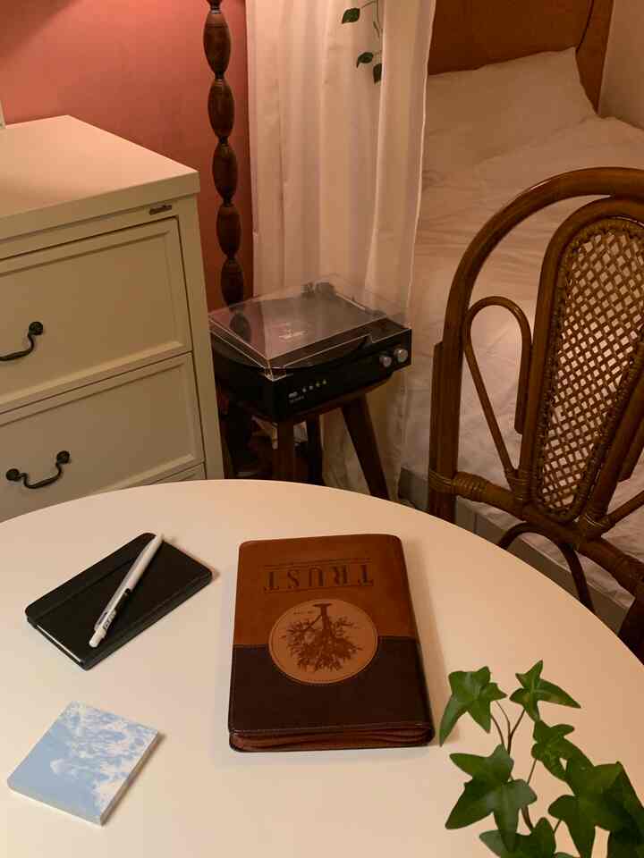 Warm brown and white toned bedroom featuring a round table with a notebook and leather organizer on top creating a vintage atmosphere