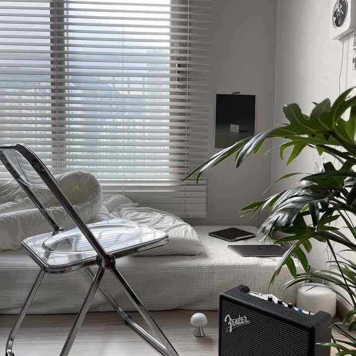 White-toned small studio bedroom featuring a transparent chair and music equipment, creating a clean and natural atmosphere