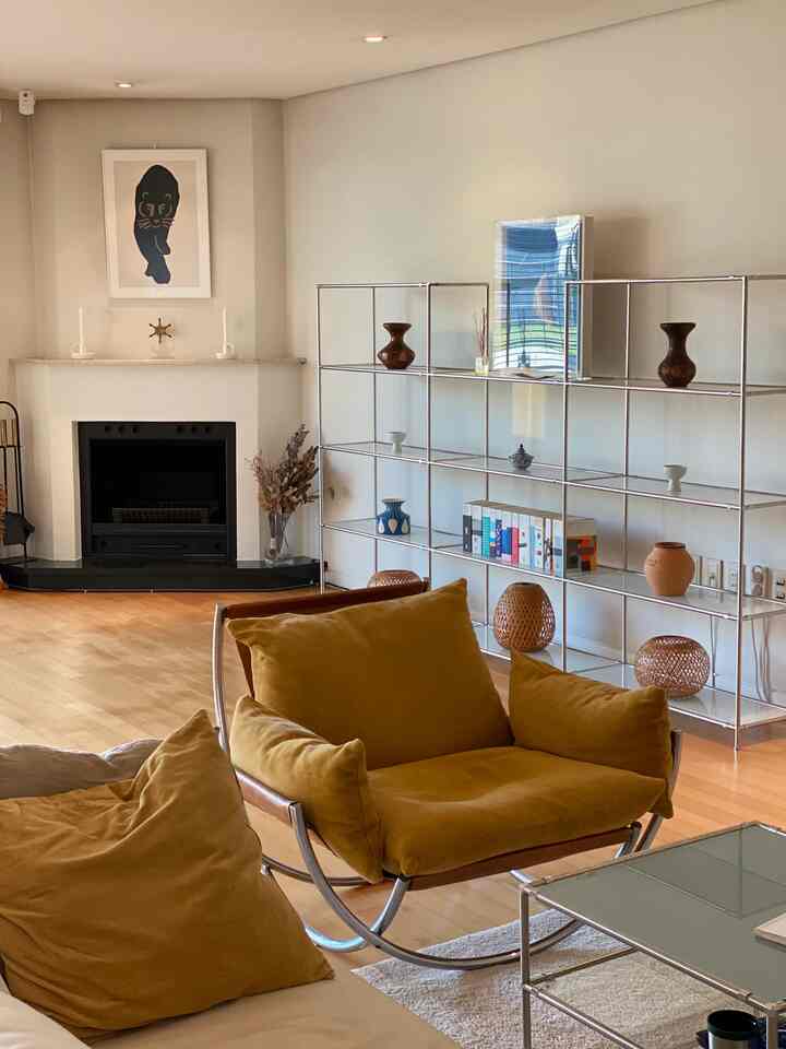 明るい白い壁と木目調の床に黄色のヴィンテージラウンジチェアと金属製の棚が配置されたモダンなリビングルーム。